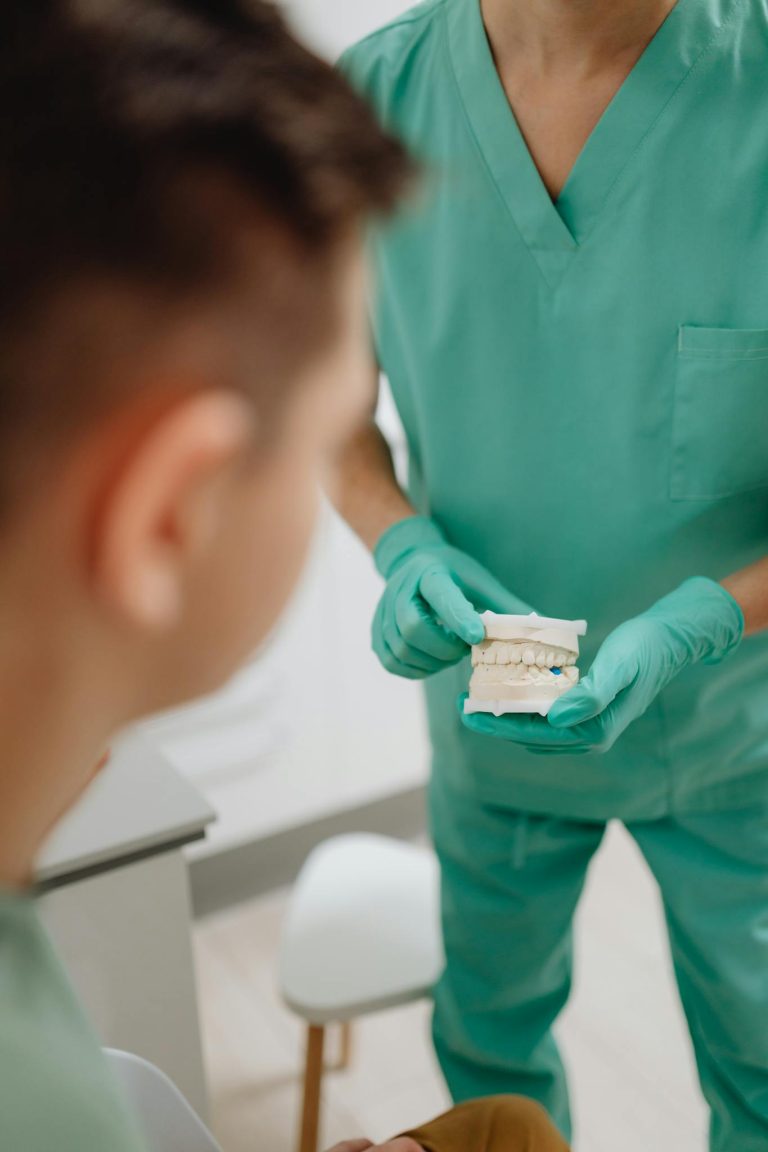 A dentist in scrubs explaining a dental model to a patient in a clinic setting.